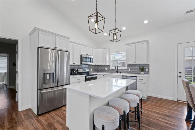 a kitchen with stainless steel appliances a refrigerator a stove a sink a center island a dining table and chairs