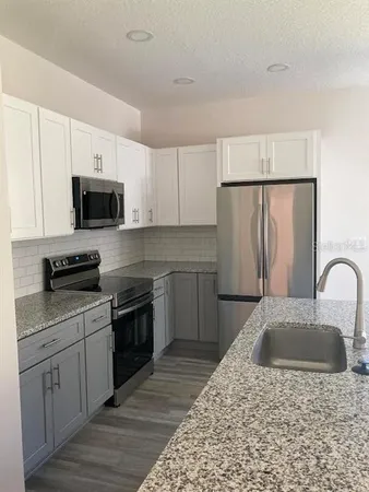 a kitchen with stainless steel appliances granite countertop a stove top oven a sink dishwasher and a refrigerator with wooden floor