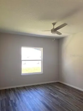 an empty room with wooden floor ceiling fan and window