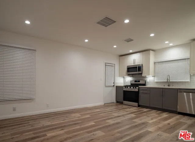 a large kitchen with stainless steel appliances granite countertop a stove a sink a refrigerator and white cabinets with wooden floor