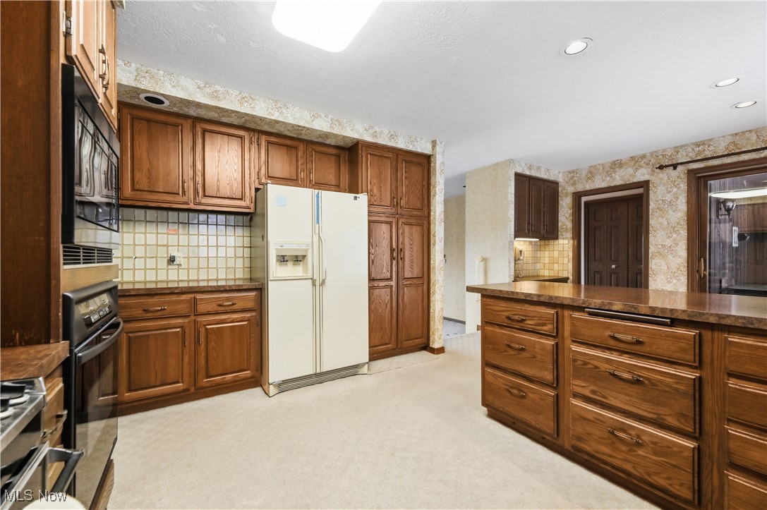 7014 River Styx Road Medina, OH 44256 - Photo 16 of 49 Kitchen featuring black appliances, light colored carpet, brown cabinets, wallpapered walls, and tasteful backsplash