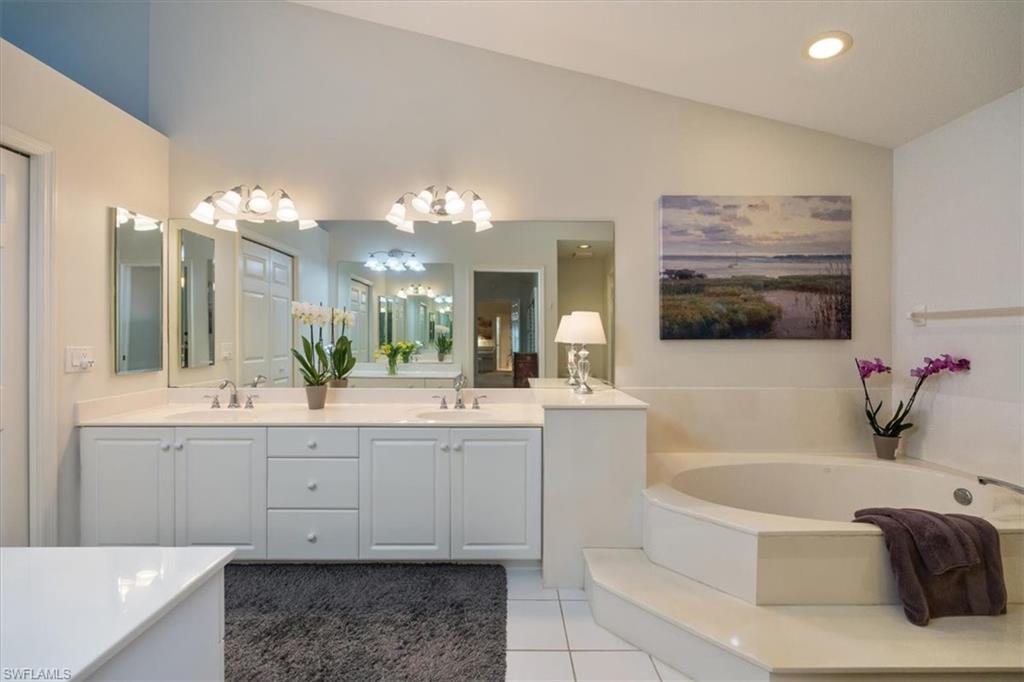 203 Via Perignon, Unit 24 Naples, FL 34119 - Photo 18 of 26 The primary bath offers dual vanities, a luxurious soaking tub, and a separate glass-enclosed shower, all opening to a spacious walk-in closet illuminated by a large window and abundant natural light.