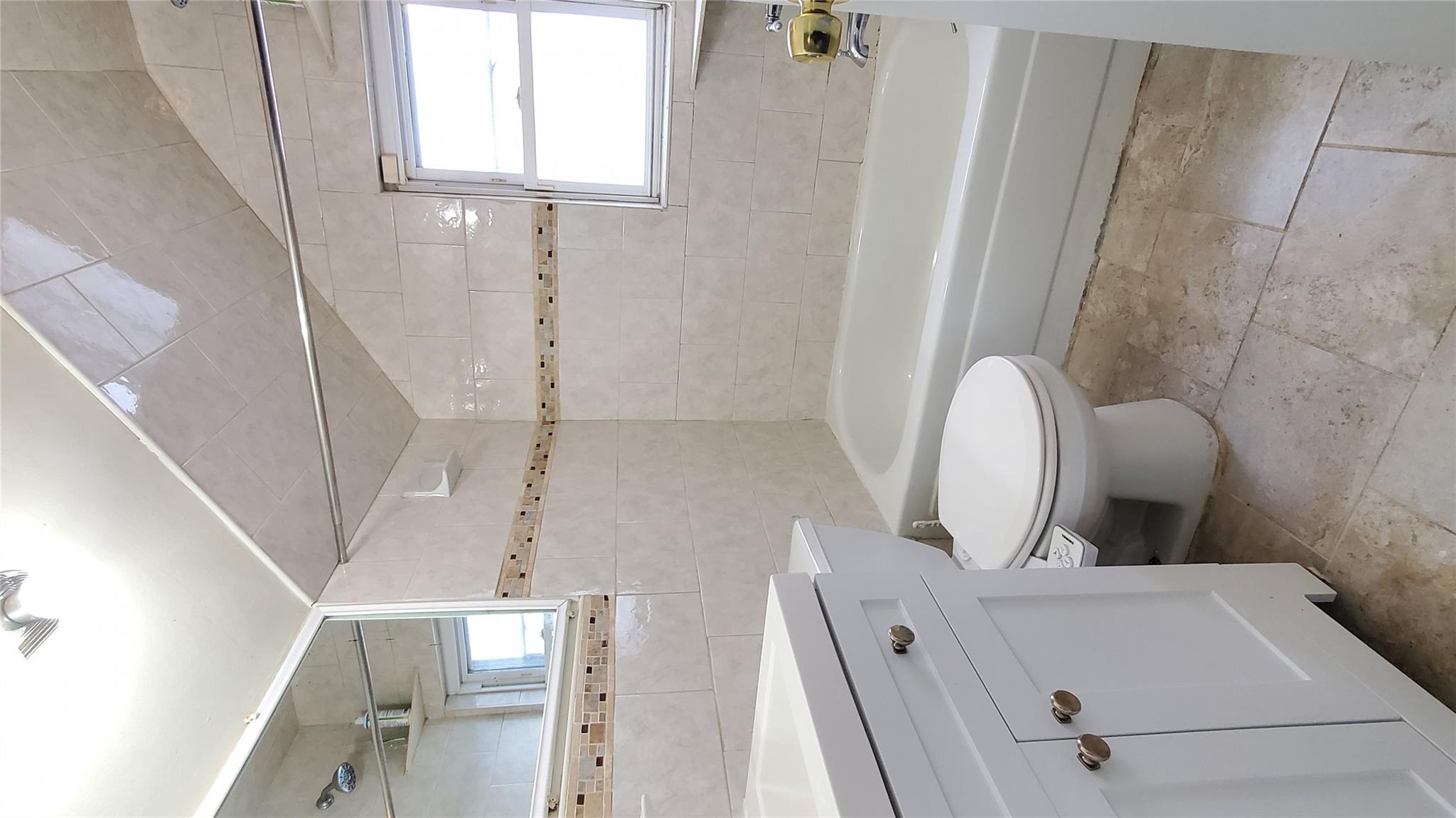 144-49 166th Street Queens, NY 11434 - Photo 9 of 15 Full bath with tile walls, shower / tub combination, toilet, vanity, and vaulted ceiling