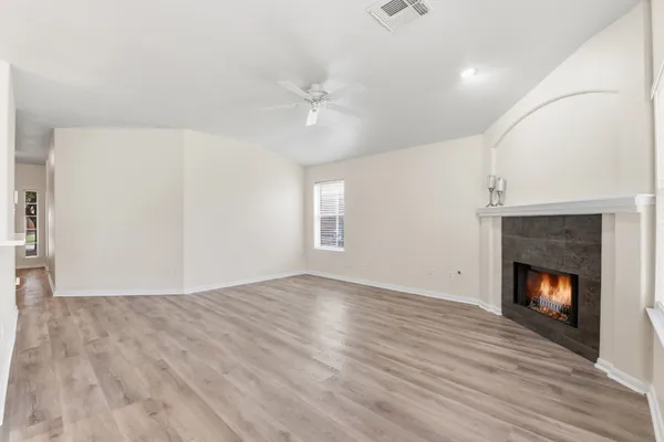 a view of an empty room with wooden floor fireplace and a window