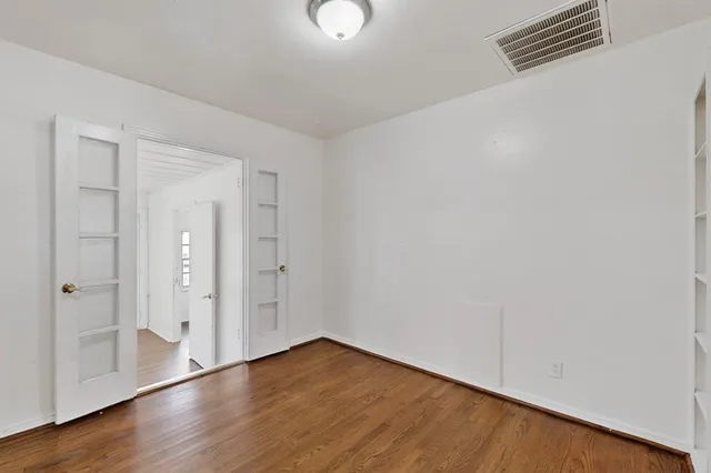 a view of an empty room with wooden floor and mirror