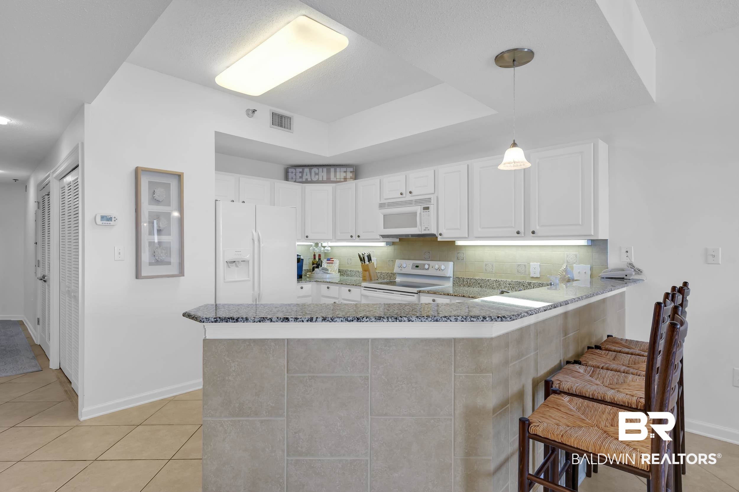 27282 Canal Road, Unit 104 Orange Beach, AL 36561 - Photo 17 of 79 Kitchen featuring hanging light fixtures, light tile patterned floors, dark stone countertops, a peninsula, and tasteful backsplash
