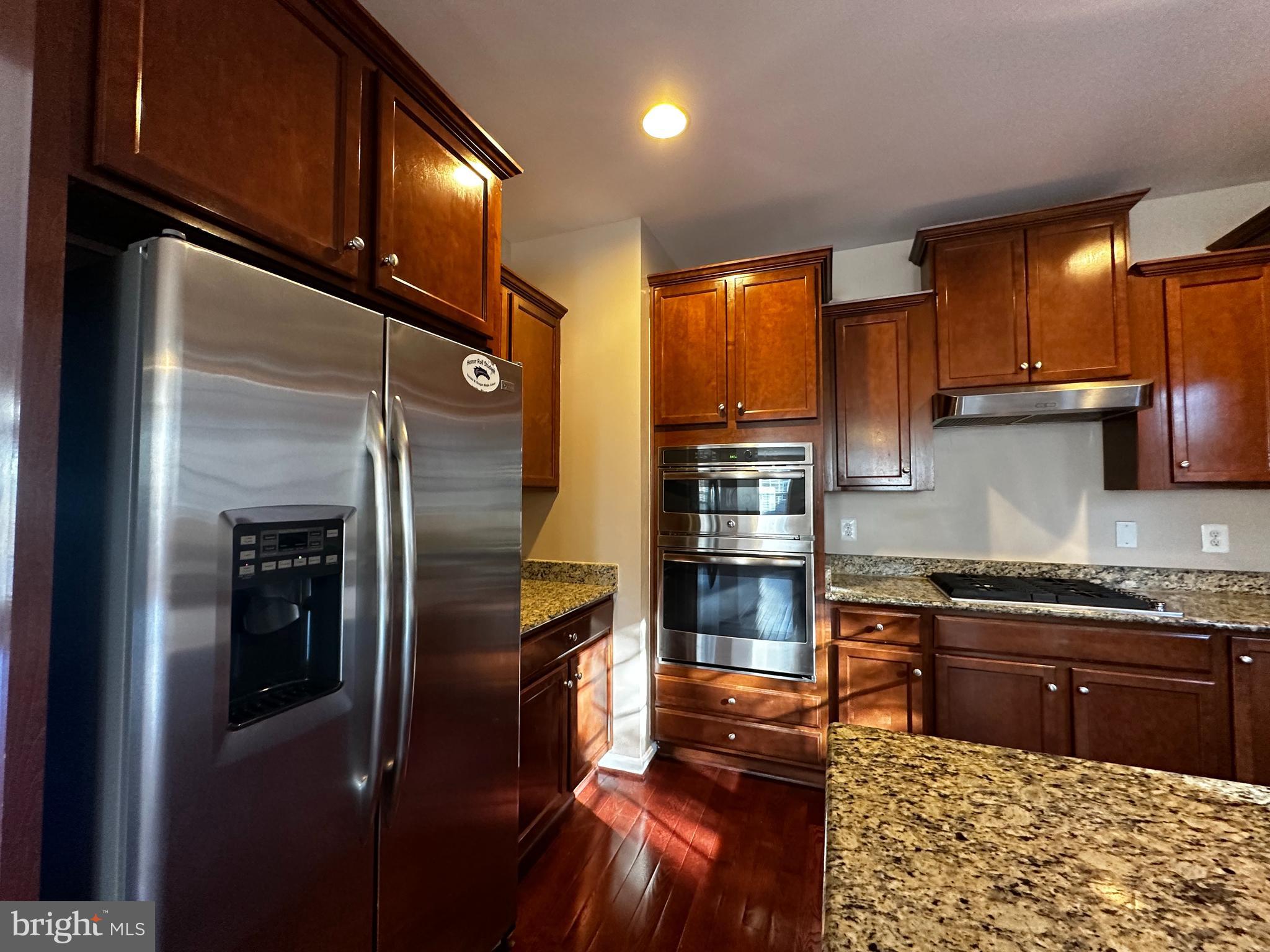 15165 Santander Drive Gainesville, VA 20155 - Photo 12 of 35 a kitchen with stainless steel appliances kitchen island granite countertop a refrigerator a stove and a sink with wooden floor