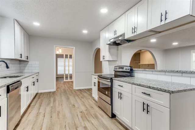 a kitchen with granite countertop a sink stainless steel appliances and white cabinets