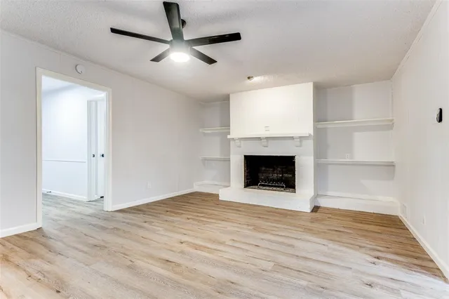 a view of an empty room with wooden floor a fireplace and a window