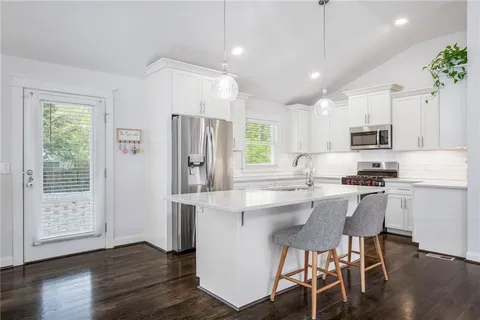 a kitchen with stainless steel appliances granite countertop a refrigerator a sink dishwasher a stove a dining table and chairs with wooden floor