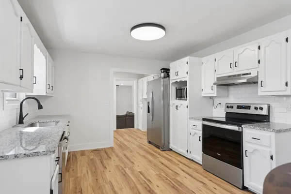 a kitchen with stainless steel appliances granite countertop a stove top oven a sink dishwasher and a refrigerator with wooden floor