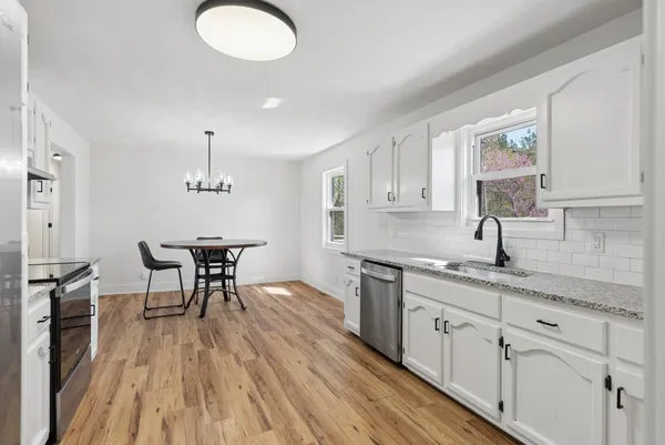 a kitchen with stainless steel appliances granite countertop a sink a stove a dining table and chairs with wooden floor
