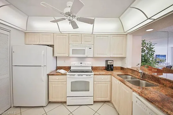 a white kitchen with granite countertop a sink a refrigerator a stove a washer dryer and cabinets