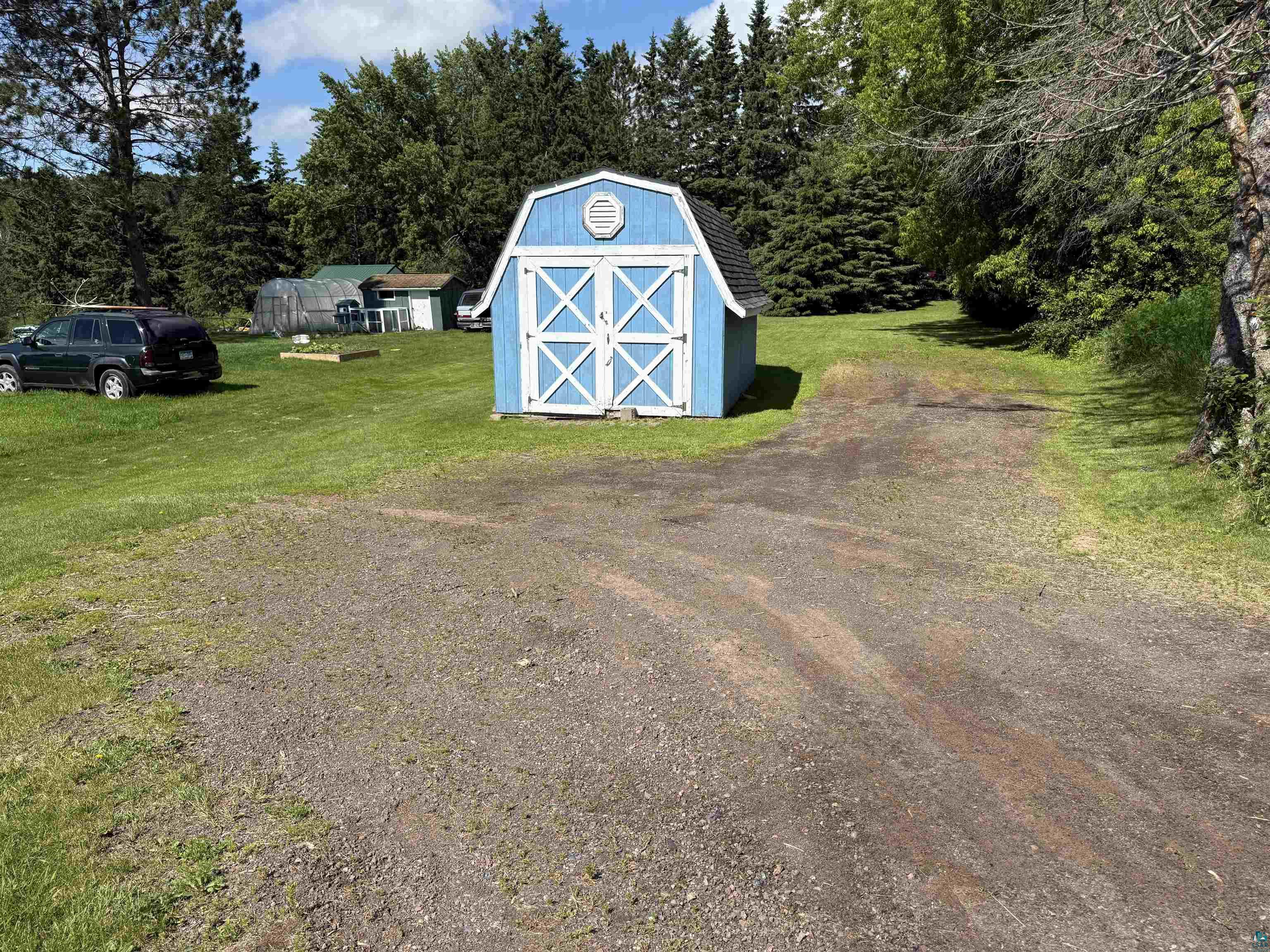 3841 Haines Road Hermantown, MN 55811 - Photo 10 of 11 Light blue barn-style shed with white trim and cross-brace doors, situated on a grassy lot with a gravel driveway