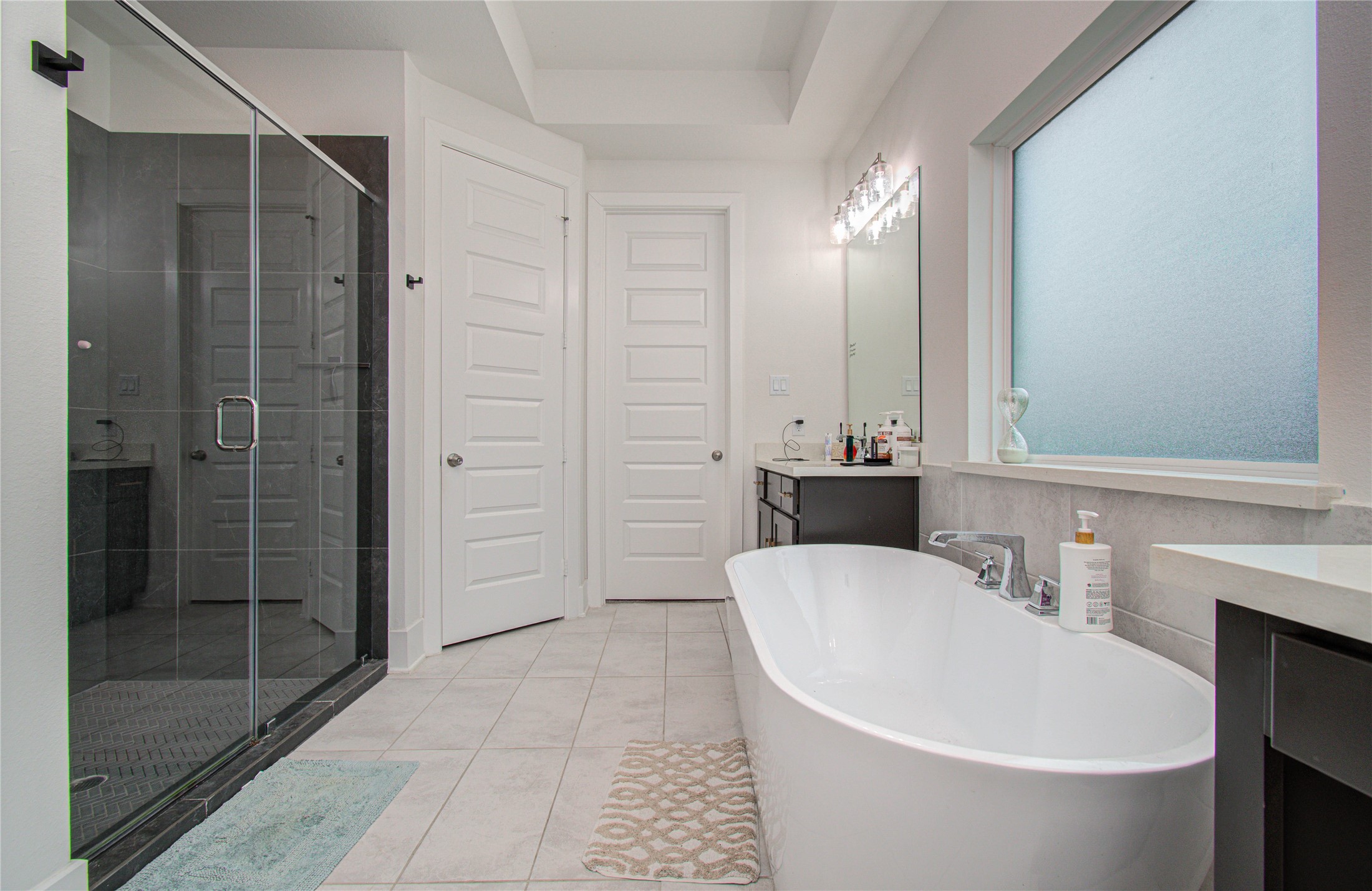 4211 Limestone Terrace Manvel, TX 77578 - Photo 19 of 33 This photo showcases a modern bathroom with a sleek design, featuring a large glass-enclosed shower, a freestanding bathtub, and a spacious vanity with ample storage. The room is bright, thanks to a frosted window, and has a clean, minimalist aesthetic.