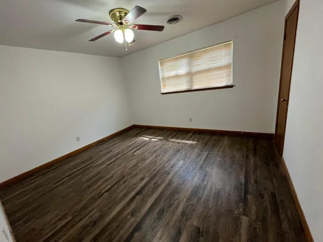 an empty room with wooden floor chandelier fan and windows