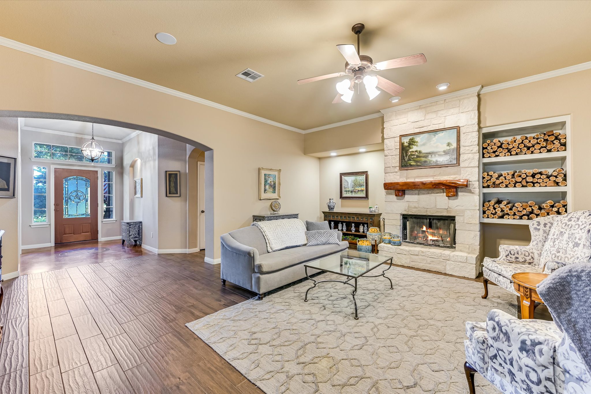 786 Ranchers Club Lane Driftwood, TX 78619 - Photo 7 of 33 Living area with wood finished floors, crown molding, a ceiling fan, arched walkways, and a stone fireplace