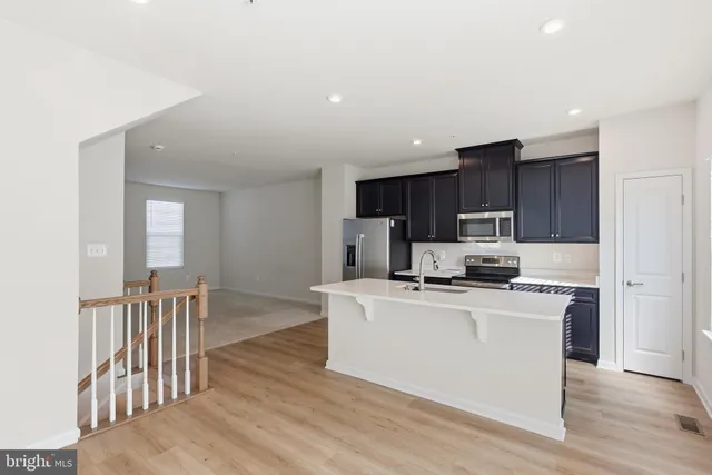 a kitchen with stainless steel appliances a stove top oven a refrigerator a sink and white cabinets with wooden floor