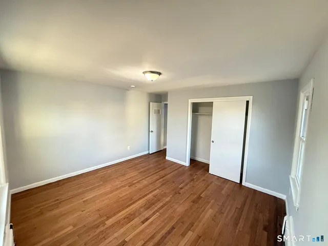 a view of an empty room with wooden floor and closet