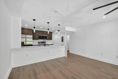 a view of a kitchen with kitchen island a sink wooden floor and black appliances
