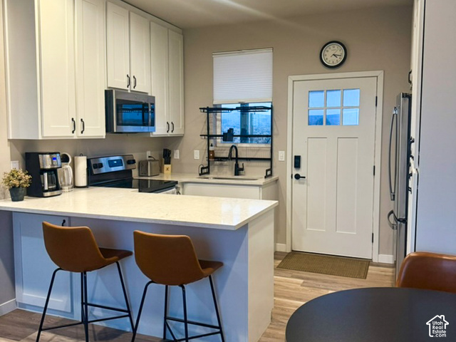 215 South Copper Road East Kanab, UT 84741 - Photo 35 of 41 Kitchen featuring light-toned cabinetry with dark hardware, stainless steel appliances, a kitchen island with seating, a window above the sink, and wood-finish flooring