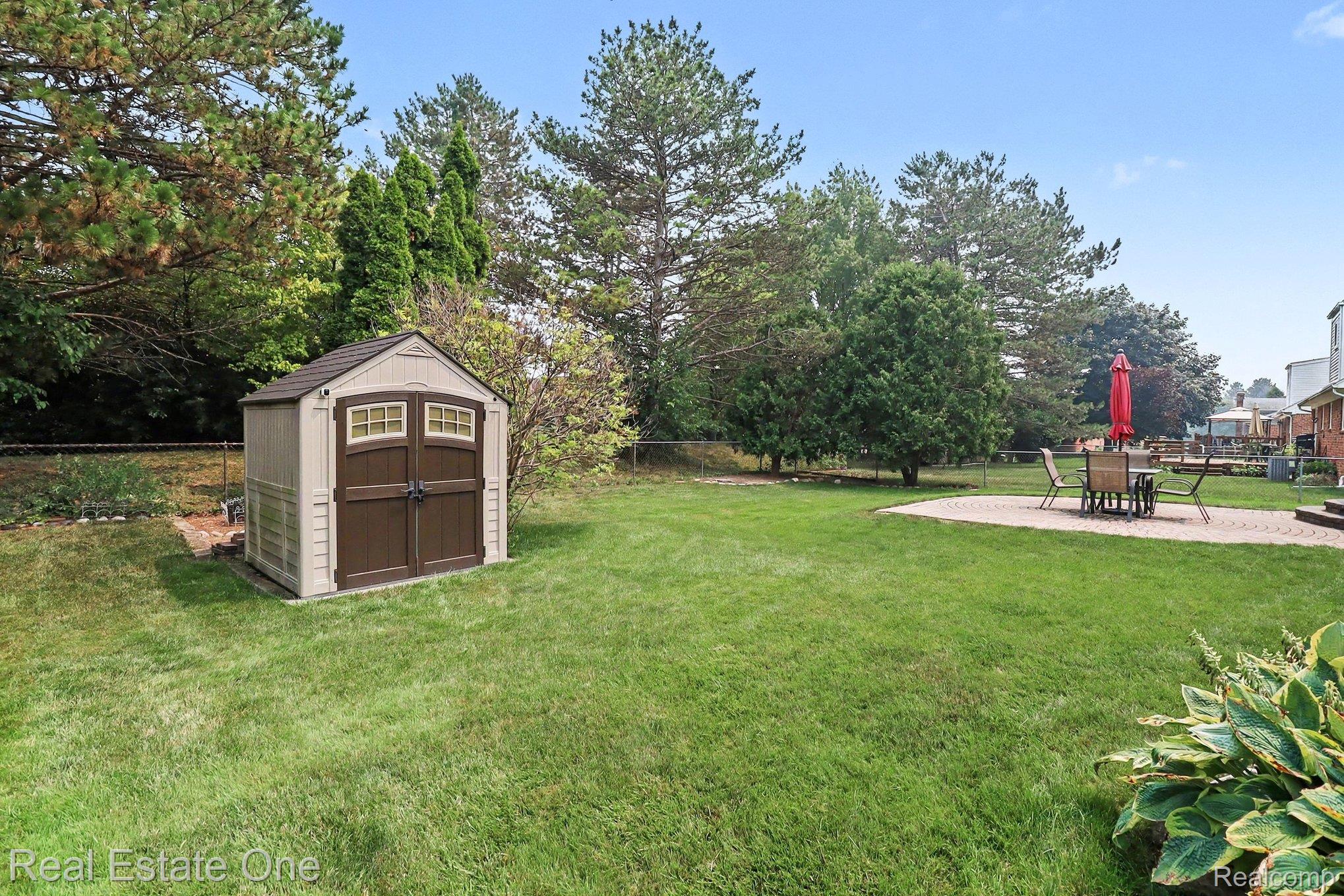 6570 Edgewood Road Canton, MI 48187 - Photo 18 of 22 Spacious lawn featuring a durable storage shed with double doors and window accents, a stone patio, and mature perimeter trees