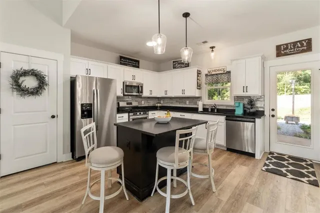 a kitchen with stainless steel appliances kitchen island granite countertop a sink a stove a refrigerator and white cabinets with wooden floor