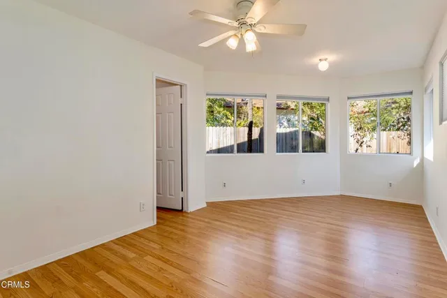 an empty room with wooden floor fan and windows