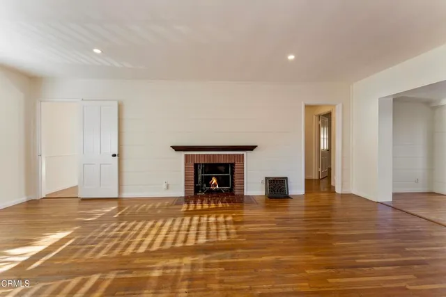 a view of an empty room with wooden floor fireplace and a window