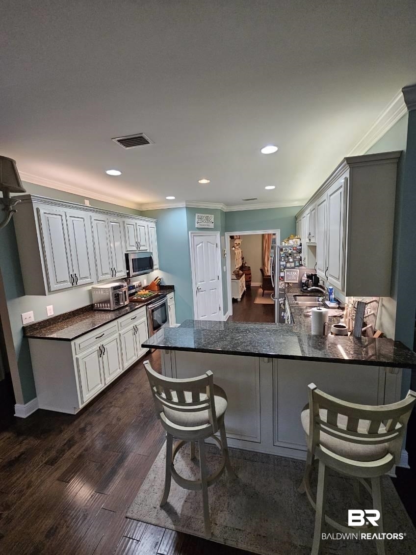 41416 Davis Duck Road Bay Minette, AL 36507 - Photo 31 of 72 Kitchen featuring a kitchen breakfast bar, dark hardwood / wood-style flooring, crown molding, stainless steel appliances, and kitchen peninsula