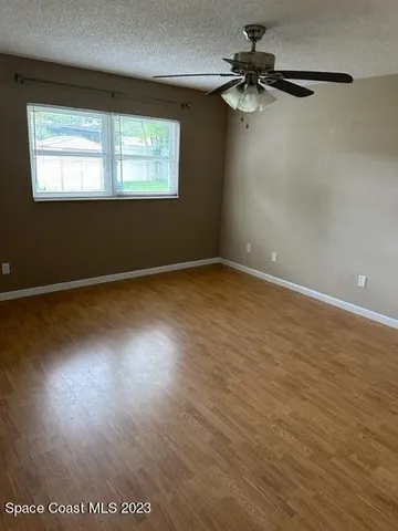 an empty room with wooden floor fan and windows