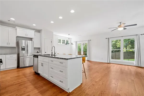 a kitchen with stainless steel appliances granite countertop a stove a sink a refrigerator and white cabinets with wooden floor