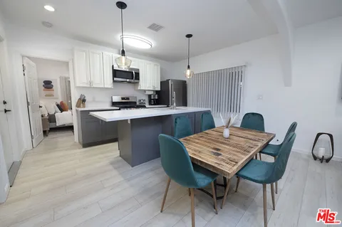 a open kitchen with stainless steel appliances granite countertop a stove top oven a sink dishwasher a dining table and chairs with wooden floor