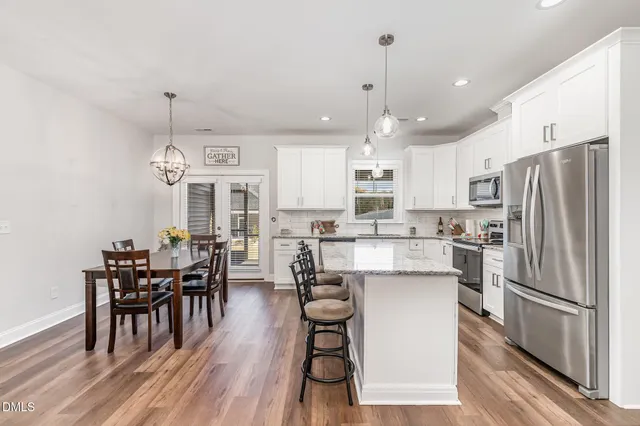 a kitchen with stainless steel appliances granite countertop a dining table chairs refrigerator and sink