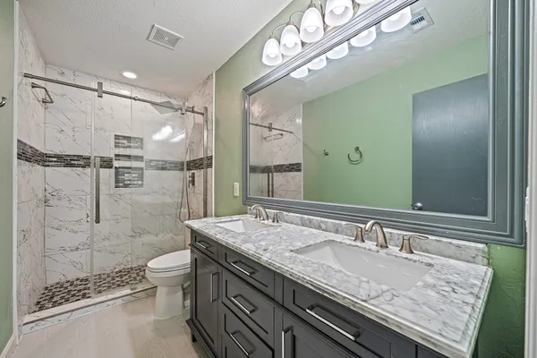a bathroom with a granite countertop double vanity sink mirror and shower