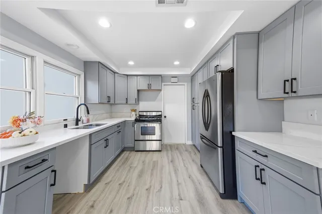 a kitchen with stainless steel appliances a sink dishwasher a refrigerator and a stove with wooden floors