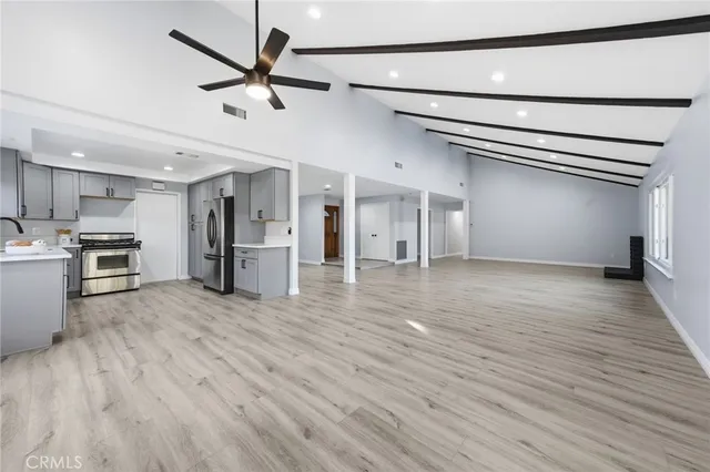 a view of an empty room and kitchen view with wooden floor