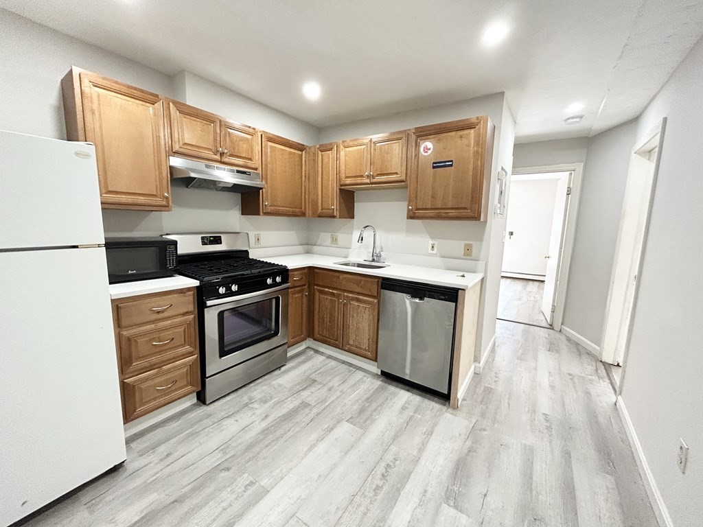 a kitchen with stainless steel appliances granite countertop a stove a sink dishwasher a refrigerator white cabinets and wooden floor next to a window