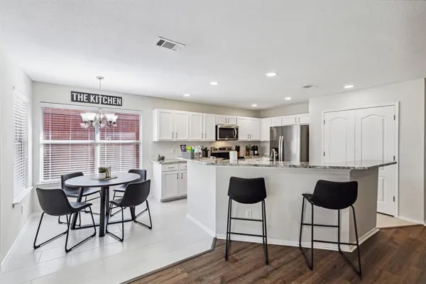 a kitchen with stainless steel appliances kitchen island granite countertop a dining table chairs and a refrigerator