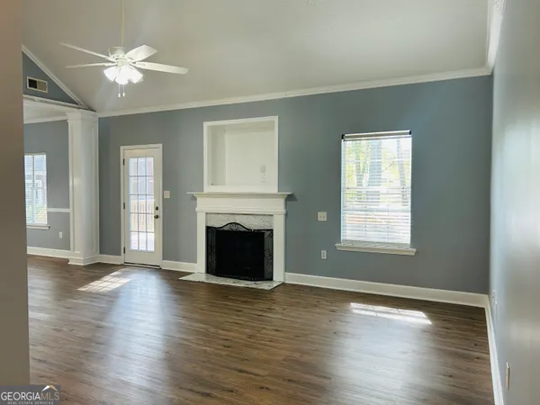 an empty room with wooden floor a chandelier fan and windows