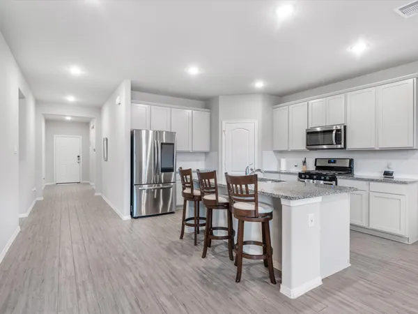 a kitchen with stainless steel appliances kitchen island granite countertop a stove a sink a refrigerator and white cabinets with wooden floor