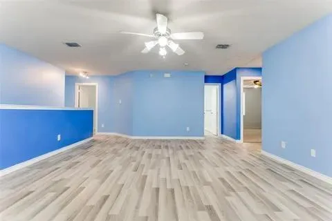 a view of an empty room with wooden floor and a ceiling fan