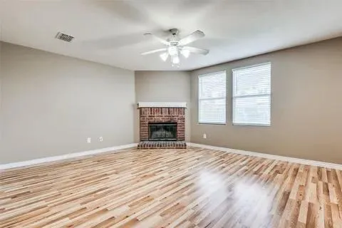 a view of an empty room with wooden floor fireplace and a window