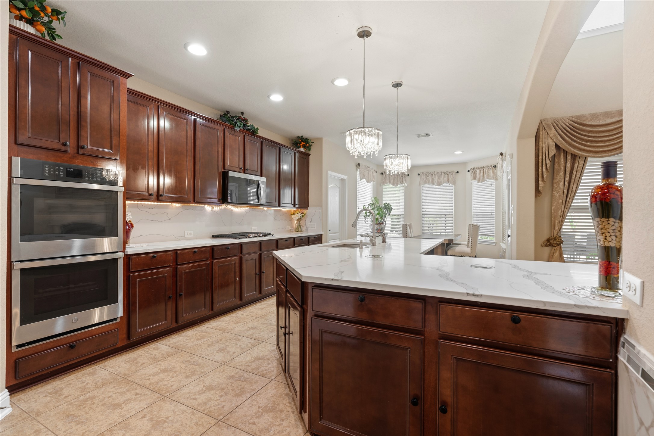 5802 Layton Meadows Lane Spring, TX 77379 - Photo 15 of 42 Kitchen with double ovens. Shows the full wall of appliances — stainless double ovens, built-in microwave, dark wood cabinetry, marble backsplash, and island.