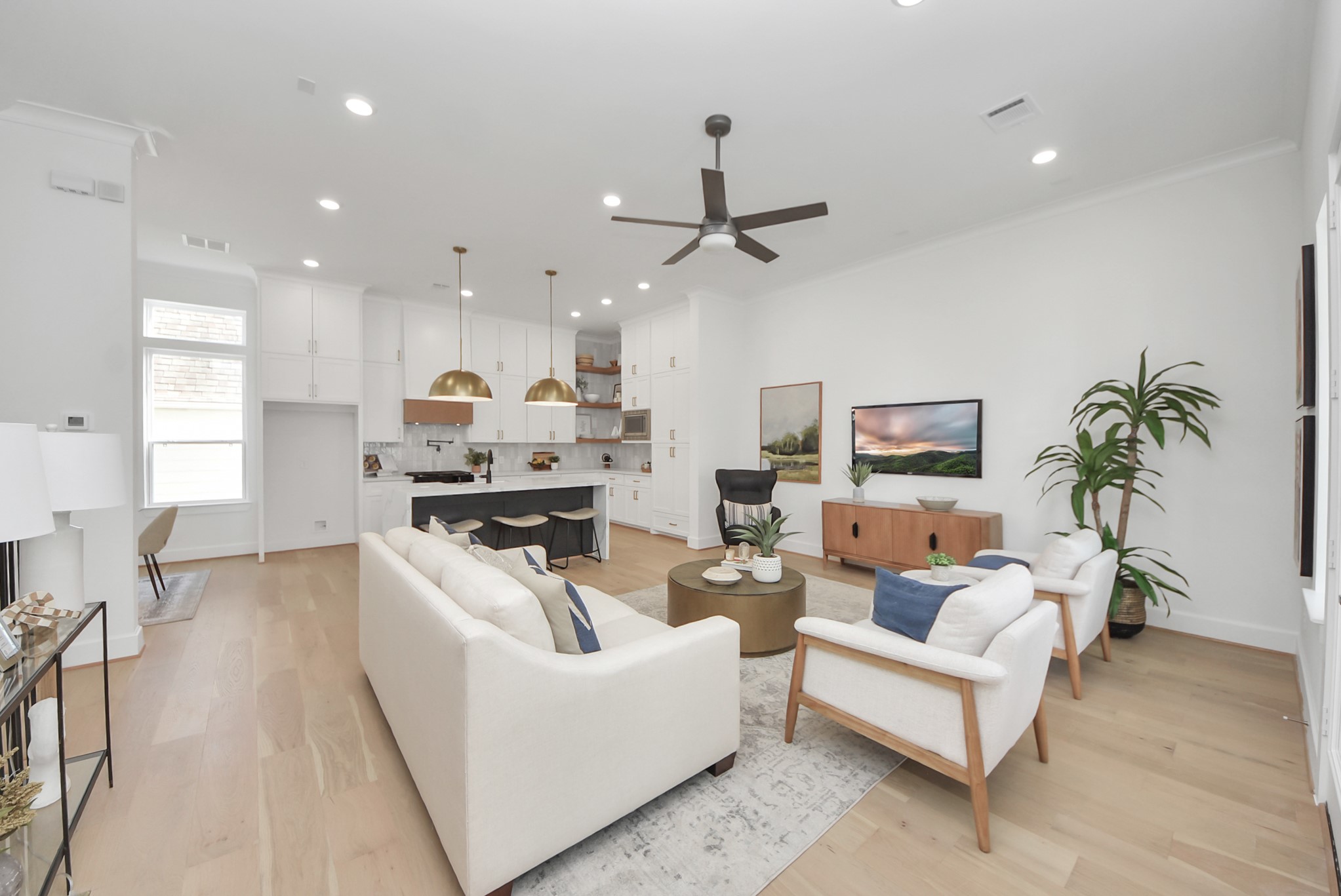 927 Fisher Street, Unit B Houston, TX 77018 - Photo 13 of 47 Welcome to this modern, open-concept living area, where light wood flooring and abundant natural light create a bright and inviting atmosphere. The sleek kitchen, with white cabinetry and gold pendant lights, flows seamlessly into a cozy living space featuring contemporary furniture and a ceiling fan—perfect for entertaining or relaxing with family and friends.