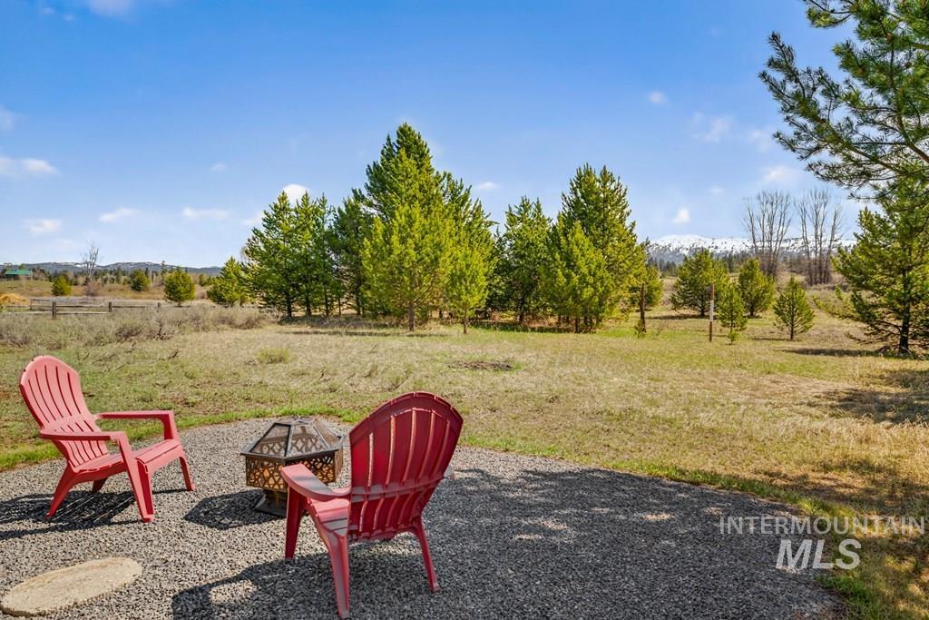 13800 Raptor Loop McCall, ID 83638 - Photo 27 of 34 Gravel patio with a metal fire pit, surrounded by a natural landscape with mature evergreen trees and distant snow-capped mountains