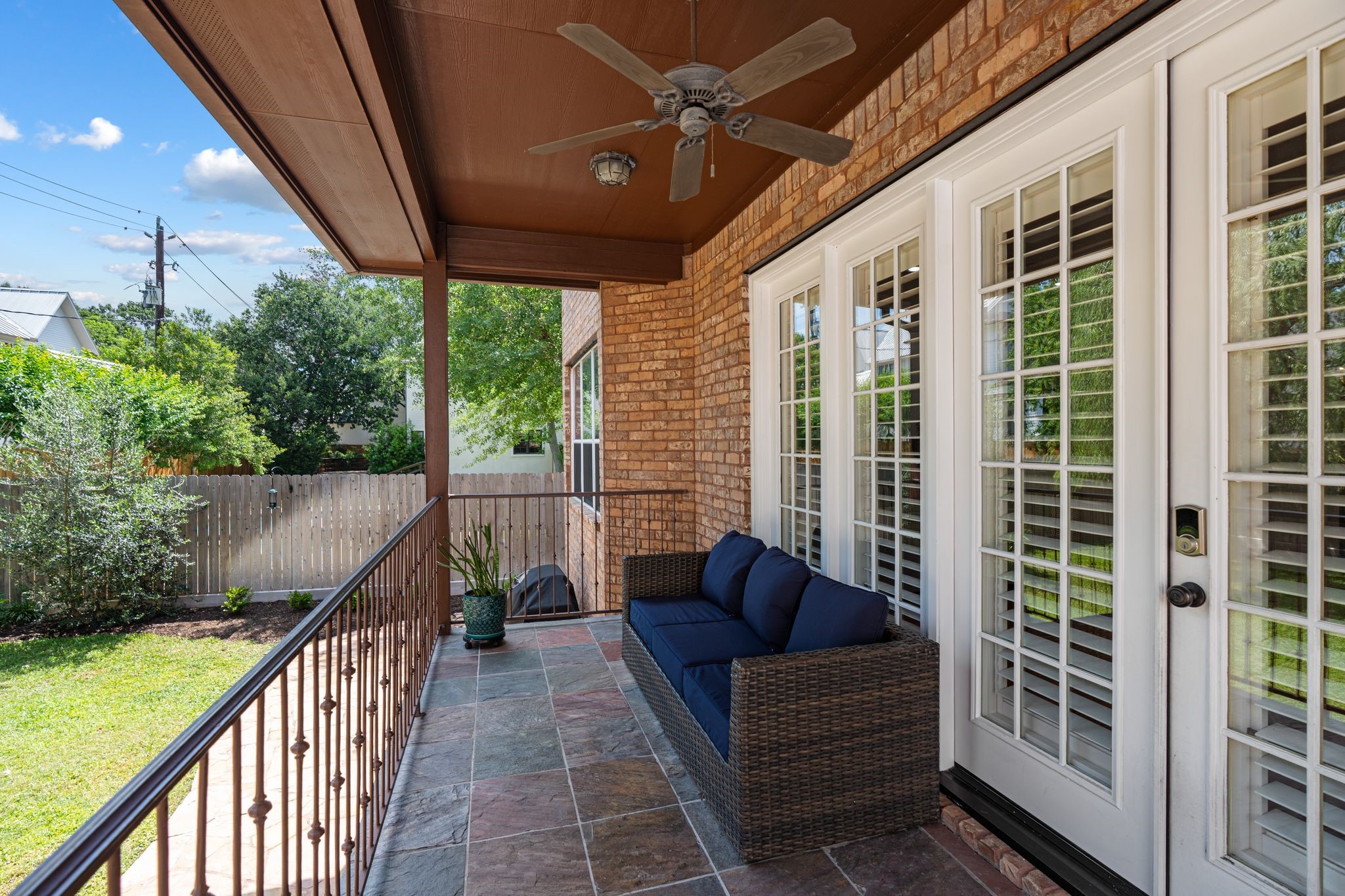3822 Merrick Street Houston, TX 77025 - Photo 30 of 34 Step out from the main living level onto the covered back porch, where a stained wood ceiling, ceiling fan, and slate tile flooring create a true outdoor living space. Ornamental iron railings frame the perimeter, and the view opens up to the lush backyard below, with a mature weeping willow adding natural privacy along the fence line.