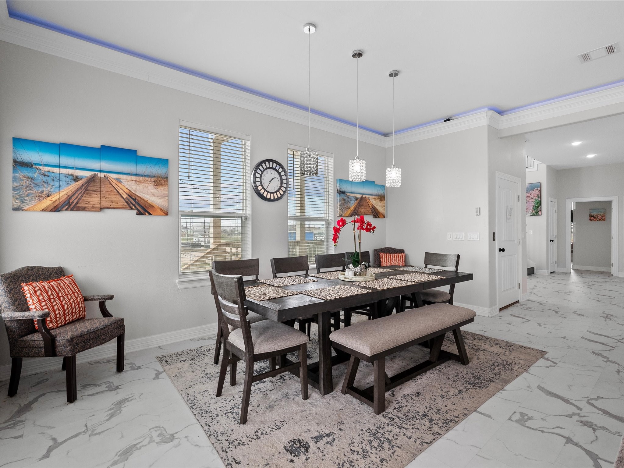 1018 Seashell Drive Surfside Beach, TX 77541 - Photo 21 of 49 This dining area features modern decor with a spacious table, bench seating, and cushioned chairs. The room is bright, with large windows, stylish pendant lighting, and marble-style flooring. Wall art and a large clock add character.