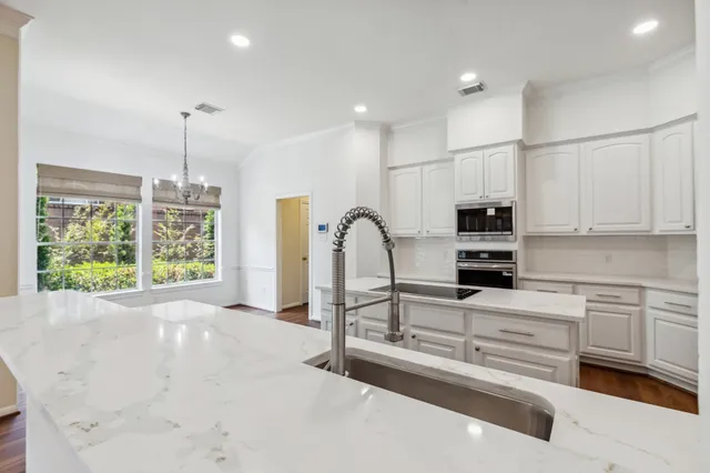 a large kitchen with stainless steel appliances refrigerator a microwave oven a stove and white cabinets with wooden floor