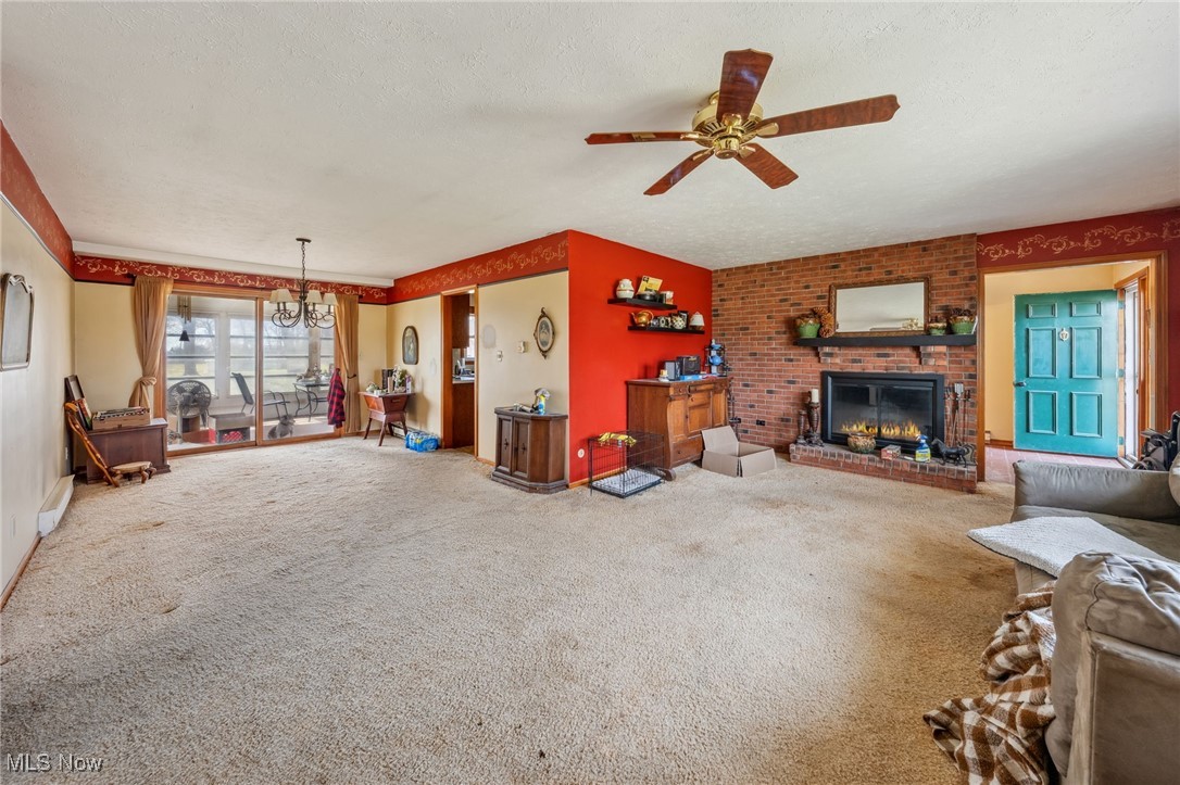 4790 Paradise Road Seville, OH 44273 - Photo 19 of 45 Unfurnished living room featuring carpet flooring, a textured ceiling, ceiling fan with notable chandelier, and a brick fireplace